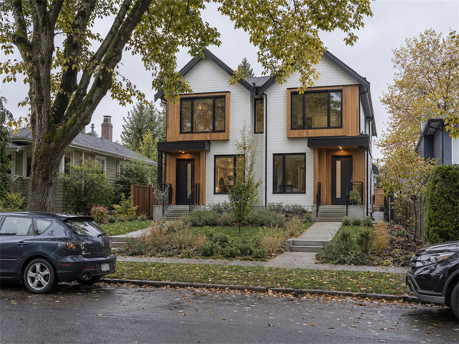A modern duplex with white siding and cedar accents on a tree-lined street in autumn