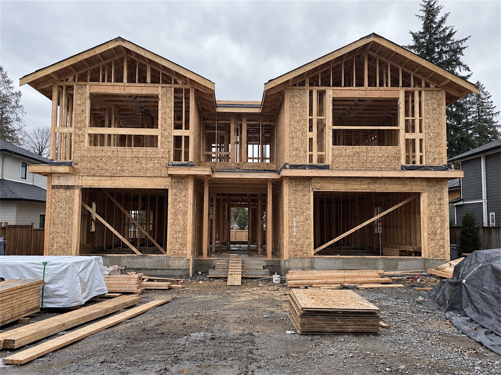 A two-storey duplex at the framing stage, with lumber stacked on site